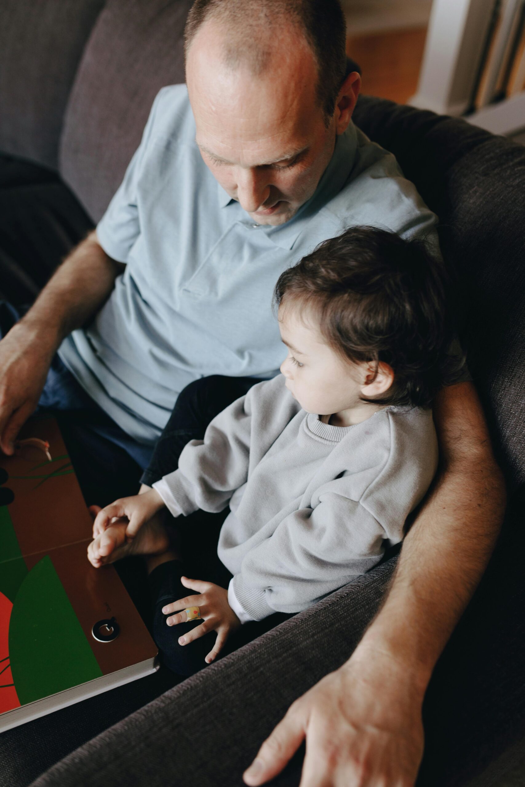 pexels-pnw-prod-7677773 Father Holding A Book Beside His Child